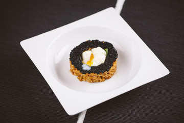 Rice dish with black caviar and egg served on a plate on a wooden table. Black background.