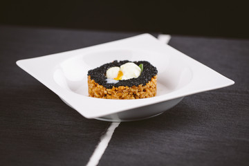 Rice dish with black caviar and egg served on a plate on a wooden table. Black background.