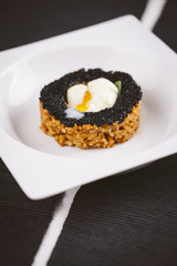 Rice dish with black caviar and egg served on a plate on a wooden table. Black background.