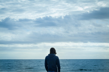 Fototapeta premium guy wearing jeans and sweater standing in front of the ocean looking the waves