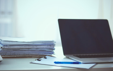 Laptop with stack of folders on table on white background