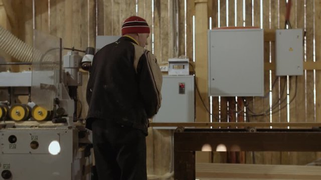 Caucasian woodworkers puts wood plank on refiner machine at sawmill, floor covered in sawdust
