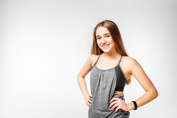 Young smiling teenage fitness girl standing against white background