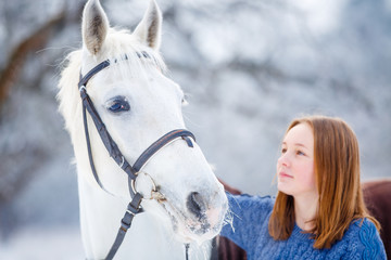 Young teenage girl portrait with white horse in winter park