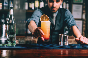 Portrait of handsome bartender serving perfect summer drink, chilled rum with orange juice and...
