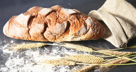 rustic crusty bread and wheat ears on a dark wooden table