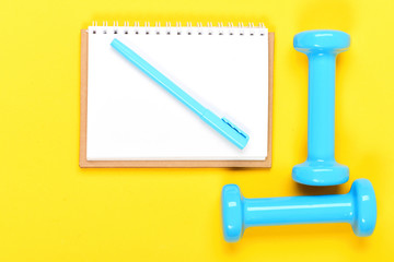 Notebook, pen and gym equipment top view on yellow background