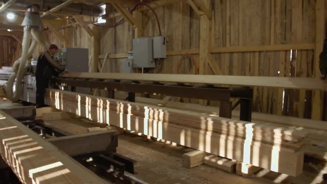 Caucasian carpenters puts wood board on jointer machine at lumber-mill, floor covered in sawdust