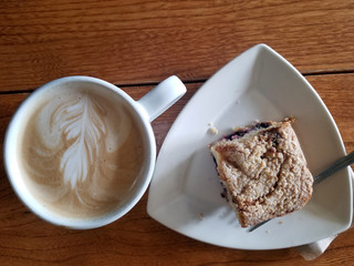 Foamy latte with latte art with blackberry lemon coffee cake on wooden table shot from above