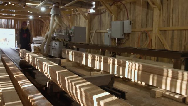 Caucasian carpenters puts wood plank on jointer machine at lumber-mill, floor covered in sawdust
