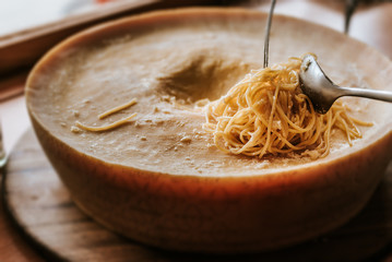 Spaghetti pasta preparation in a parmesan cheese wheel. - obrazy, fototapety, plakaty