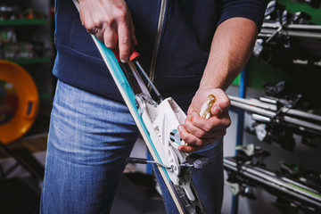 Theme tincture and repair ski equipment ski. Close-up of a Caucasian man's hand use a hand-held screwdriver tool to tweak, twist bindings for ski boots in the workshop