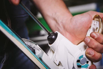 Gardinen Theme tincture and repair ski equipment ski. Close-up of a Caucasian man's hand use a hand-held screwdriver tool to tweak, twist bindings for ski boots in the workshop © Elizaveta