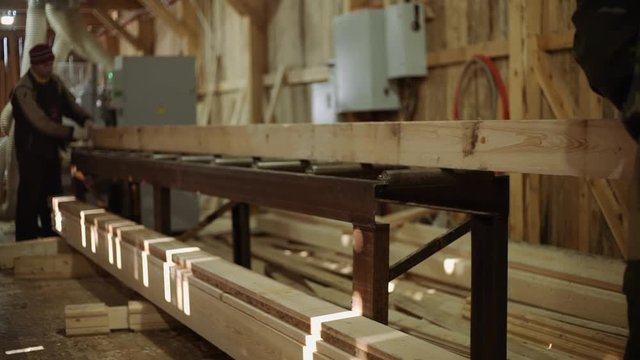 Caucasian woodworkers puts wood plank on refiner machine at sawmill, floor covered in sawdust