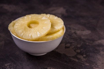 Pineapple rings in a white bowl. Canned ananas slices, copy space