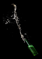 Green beer bottle opening with exploding and splashing on dark background