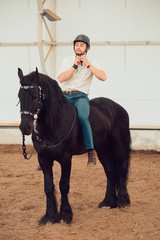 Handsome man in a shirt riding on a brown horse