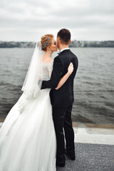Posing for the camera. Young wedding couple. Romantic Married Couple. The bride and groom stand leaning against each other. The bride with a wreath of  and a bouquet. Redhed bride haired young
