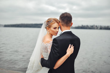 Obraz premium Posing for the camera. Young wedding couple. Romantic Married Couple. The bride and groom stand leaning against each other. The bride with a wreath of and a bouquet. Redhed bride haired young
