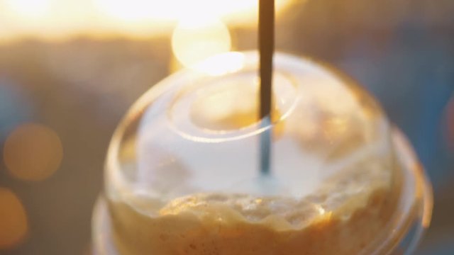 Close-up shot of cold coffee drink in takeaway cup with straw against the sunset light
