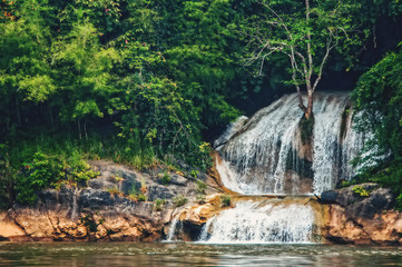 Fototapeta na wymiar Deep forest waterfall in the wild tropical forest. The shoreline of the river.
