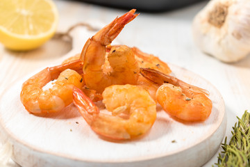 Grilled shrimps with lemon, paprika, spices and herbs on a white wooden board.