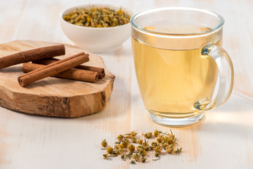 Cup of chamomile tea with dry chamomile flowers  on white wooden background.