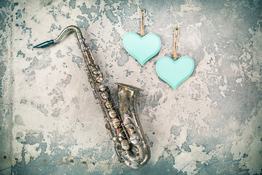 Aged retro saxophone and handmade wooden Valentine's day love hearts hanging on grunge textured concrete wall background. Vintage old style filtered photo