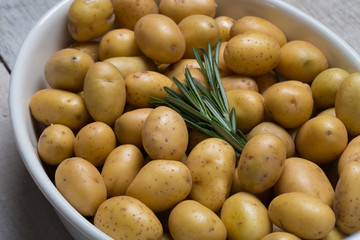 Close-up raw baby potatoes in pan with rosemary, ready to cook in oven.