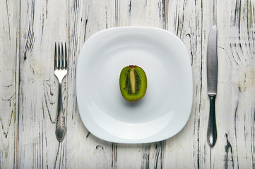 Eating for a girl, women on a strict diet. Half a juicy sweet ripe green kiwi on a white plain plate. Too little food for losing weight. Anti-obesity diet by evil nutritionist.