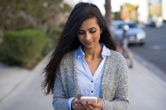 Young Indian woman walking street texting on cell phone