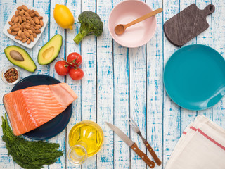 Piece of fresh salmon on a plate, avocado, almonds, sunflower oil and vegetables on a table