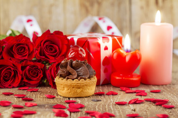 Cupcake with cherry in front of bouquet of red roses and candles. Valentines Day concept.