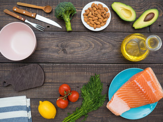 Piece of fresh salmon on a plate, avocado, almonds, sunflower oil and vegetables on a table