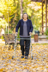 Senior woman walking with walker outdoors in autumn park