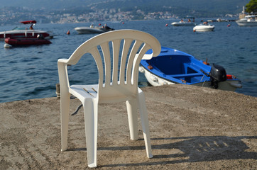 White plastic chair on a beach with a view to a sea and boats