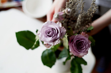 The hands of the florist with roses and decorative grasses. The preparation of the composition.