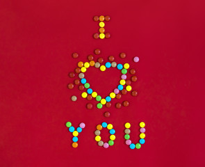 on a red background written with sweets I love you in the shape of a heart with colorful round candies 