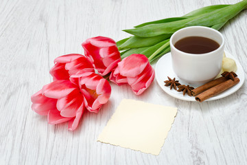Fototapeta na wymiar Pink tulips, mug of coffee and cinamon. Empty postcard. Llight wooden background.