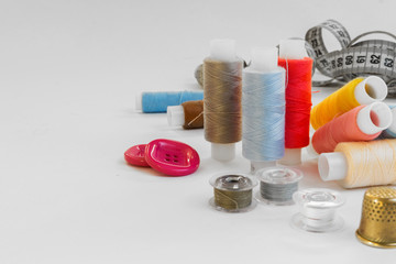 Multicolored threads, scissors, buttons, fabric and various sewing accessories on a white background with copy space flat lay