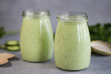 Green organic smoothies in glass jars on a gray background.