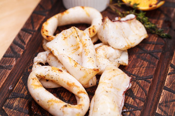 grilled squid rings on a wooden board with sauce