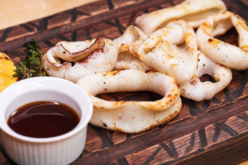 grilled squid rings on a wooden board with sauce