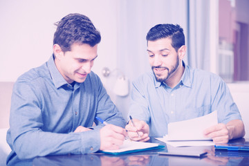 Two cheerful men reading documents at table