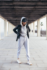 Cool and hip young female in grey fashionable tracksuit, sweatpants and hoodie poses for camera during fashion photoshoot, urban street style for social media or fashion outfit blog