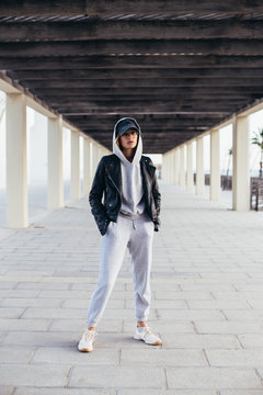 Cool and hip young female in grey fashionable tracksuit, sweatpants and hoodie poses for camera during fashion photoshoot, urban street style for social media or fashion outfit blog