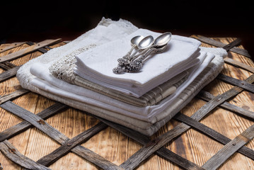 A pile of kitchen towels on wooden table with metal spoons