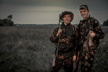 Hunters men with trophy in rural field during hunting period at dusk