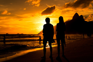 Silhouette of a Couple Walking in Ipanema Beach in Rio de Janeiro by Sunset with Mountains in...