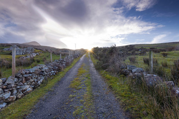 A lonely road leads into the mountains of Co. Galway Ireland with the sun coming from behind the clouds.  